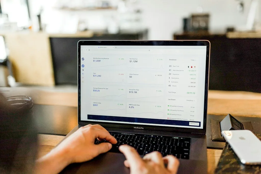 Notebook aberto em um painel de receita recorrente de um SaaS, com mãos digitando sobre uma mesa de madeira