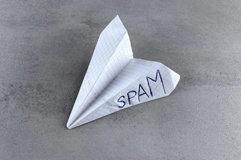 Avião de papel marcado como spam sobre uma superfície cinza