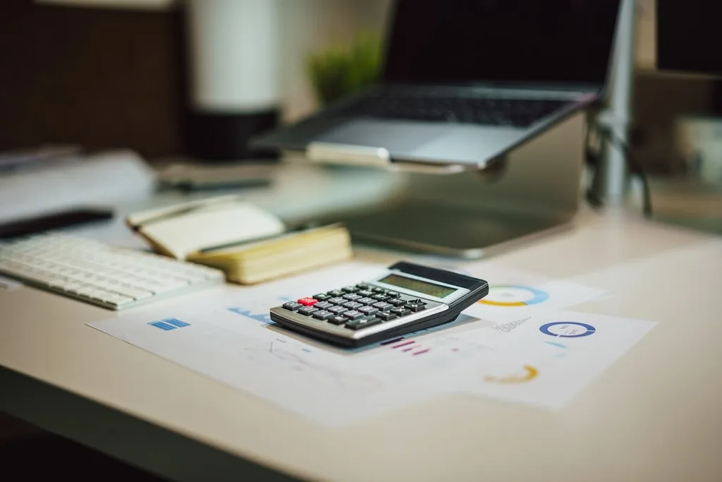 Calculadora sobre relatório financeiro ao lado de um notebook